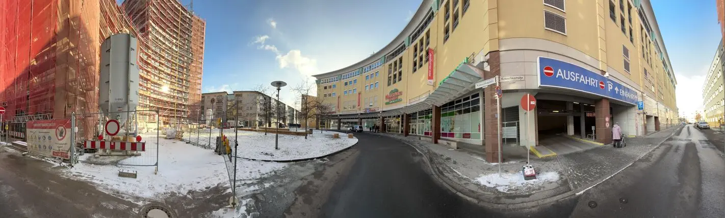 Schneebedeckte Straße in Berlin mit geschwungener Ladenzeile, Parkhauseinfahrt und rotem Baugerüst.