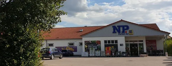 Vor einem weißen Fachmarktgebäude in Bückeburg steht das NP-Logo über dem Eingang, daneben sind Einkaufswagen, Werbeschilder und ein Auto zu sehen.