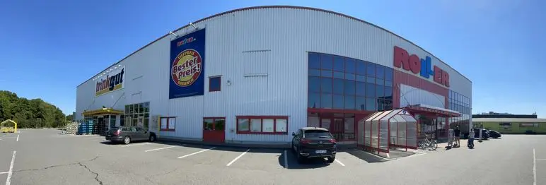 Ein großes weißes Einzelhandelsgebäude mit Roller-Schriftzug, Glasvordach und geparkten Autos auf dem Parkplatz in Hildesheim.