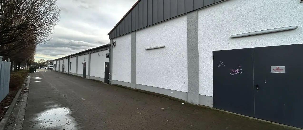 A long white commercial building with dark doors and a wet paved driveway in Minden under cloudy skies.