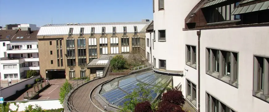 Blick auf moderne Wohn- und Geschäftsgebäude mit geschwungener Dachterrasse, Glasdach und Innenhof in Mönchengladbach an einem sonnigen Tag.
