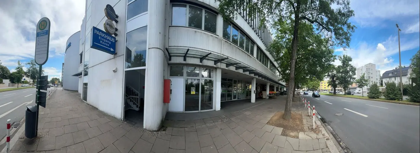 Straßenecke in Herford mit einem weißen Parkhaus, Schaufenstern, Gehweg und Stadtverkehr vor einem Bürogebäude.