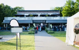 Veranstaltung im Freien mit einer großen Gruppe von Menschen vor einem Restaurant mit Sonnenschirmen und einer Terrasse.