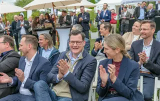 Beim Retailer Meeting am Möhnesee applaudieren die Gäste unter weißen Zelten und tauschen sich beim Branchentreffen in lockerer Runde aus.
