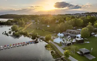 Am Möhnesee findet das Retailer Meeting bei Sonnenuntergang am Ufer statt, mit Festzelten, Stegen, Booten und weitläufiger Grünfläche.