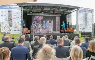 Beim Retailer Meeting am Möhnesee spricht ein Referent vor Publikum, während die Retail- und Handelsimmobilienbranche unter freiem Himmel zusammenkommt.